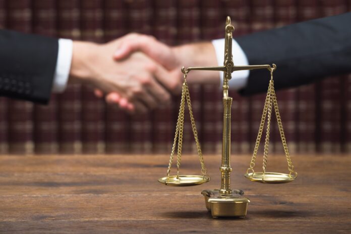 Justice Scale On Table With Judge And Client Shaking Hands